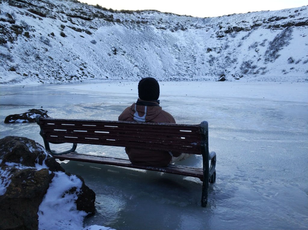 A guy sits on a bench frozen in lake kerid in the crater of an extinct vuklan. Wonders of Iceland in Winter.